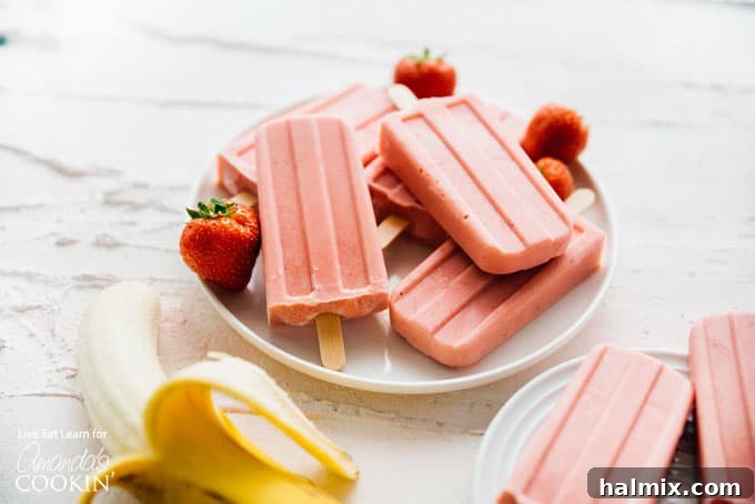 Two strawberry banana popsicles arranged artfully on a white plate, ready to be eaten.