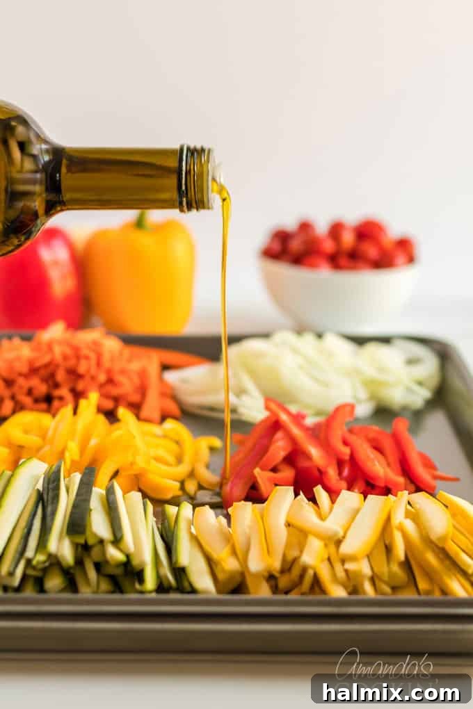 Olive oil being drizzled over a medley of julienned fresh vegetables spread across a large baking sheet, ready for roasting.