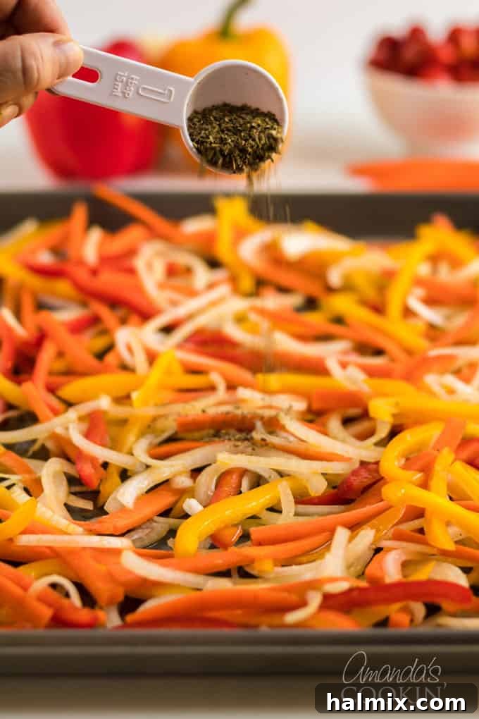 Dried Italian herbs being sprinkled over a colorful array of fresh, julienned vegetables on a baking sheet, glistening with olive oil.