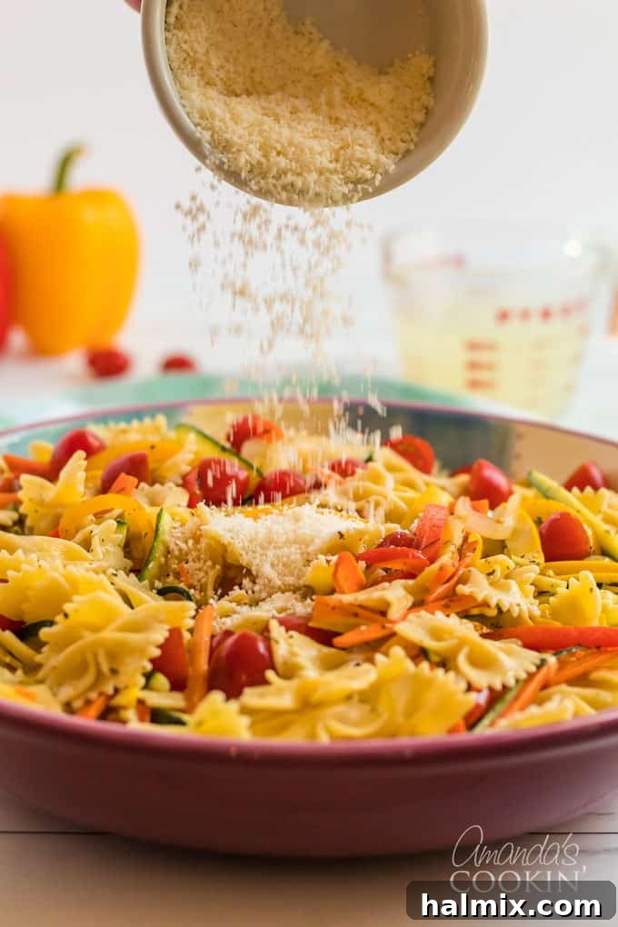 Freshly grated Parmesan cheese being generously sprinkled over a large bowl of hot Pasta Primavera, adding a savory finish.