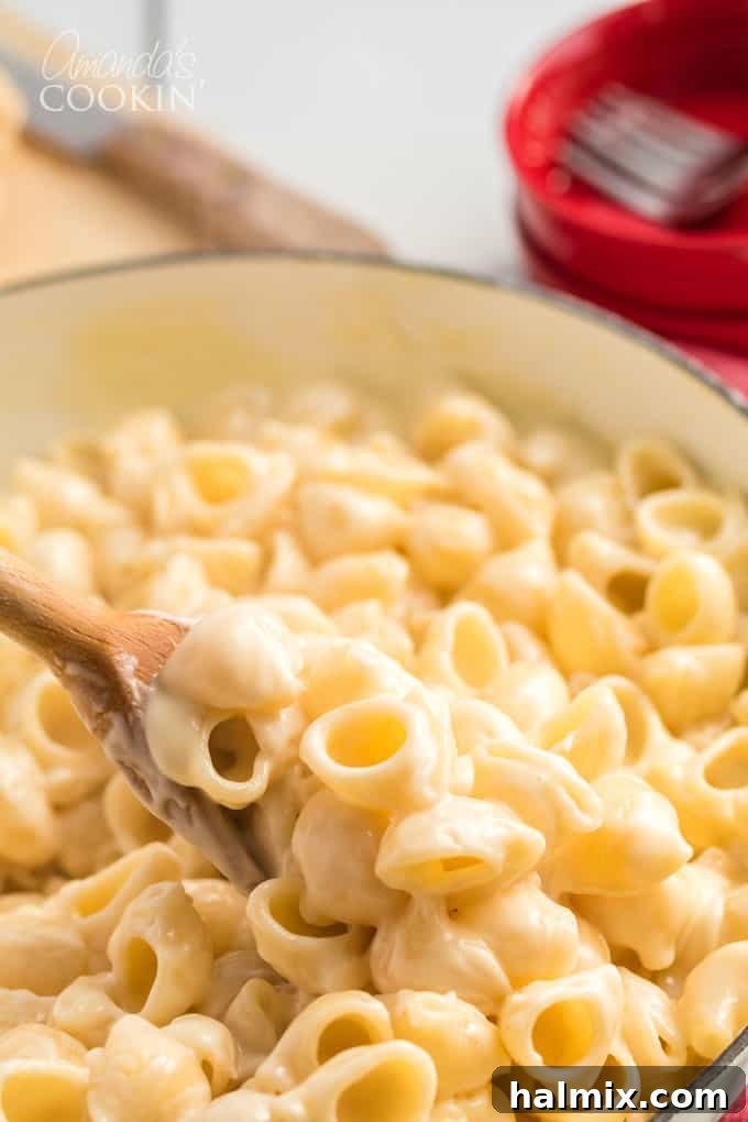 bowl of homemade panera mac and cheese being stirred with a wooden spoon, highlighting the smooth cheese sauce