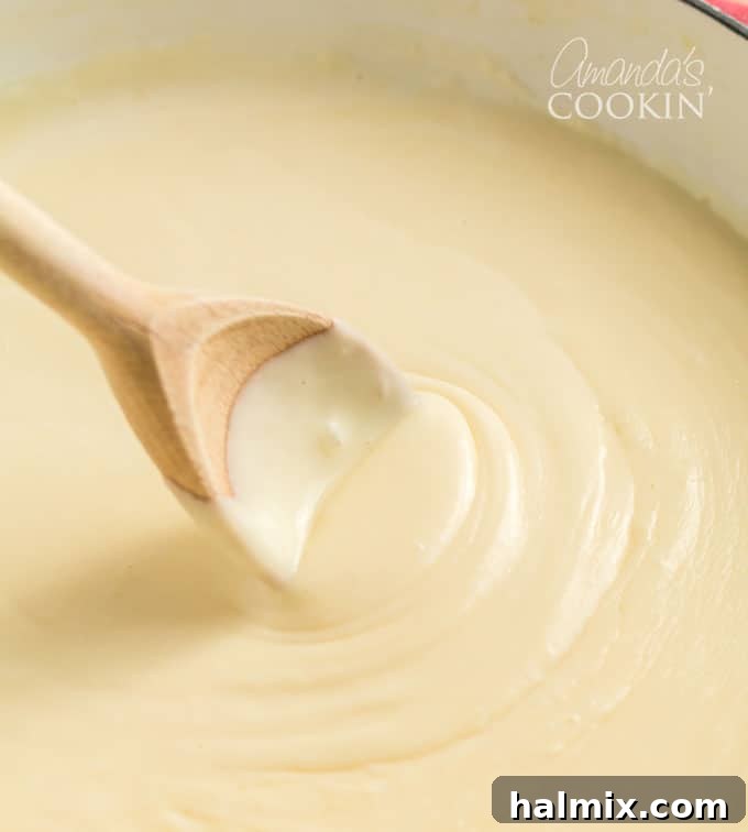 wooden spoon stirring rich, smooth cheese sauce in a saucepan