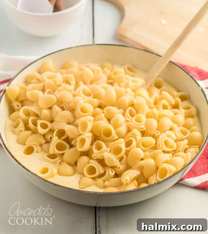 stirring cheese sauce into bowl of pasta, combining ingredients for panera mac and cheese