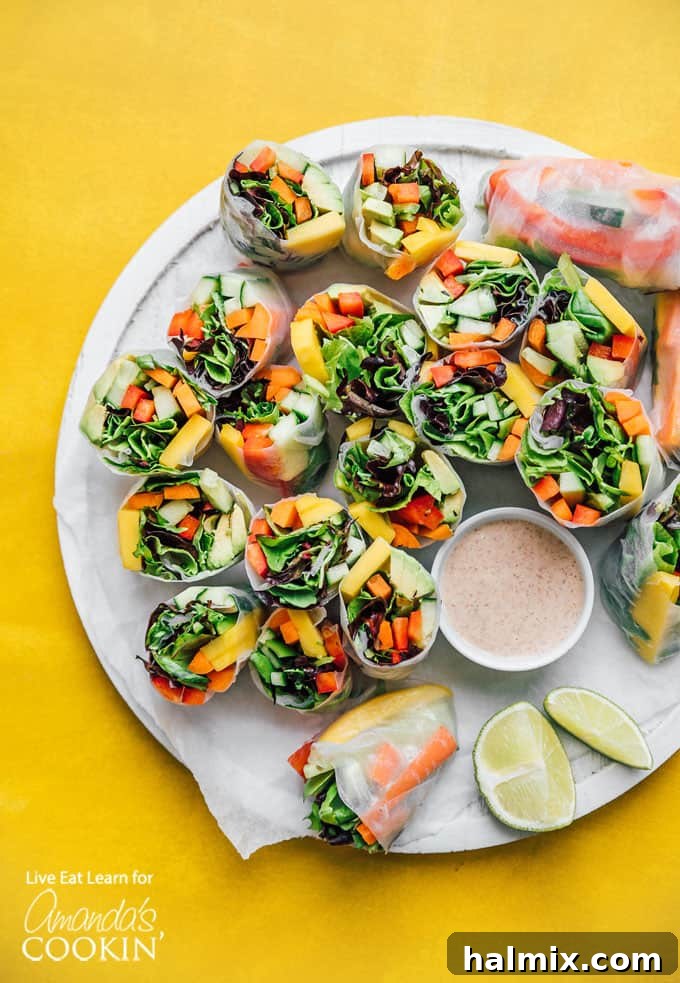 Fresh Vegetable Spring Rolls are made from colorful crisp vegetables and are a healthy appetizer that are perfect for summer! #springrolls #vegetable #veggierolls #summer #summerrecipes #potluck #avocado #jalapeno #appetizers #appetizerrecipes #vegetarian Colorful vegetable spring rolls on a plate with dipping sauce, garnished with fresh herbs and lime wedges.
