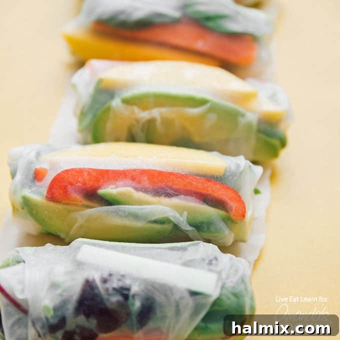 Fresh Vegetable Spring Rolls are made from colorful crisp vegetables and are a healthy appetizer that are perfect for summer! #springrolls #vegetable #veggierolls #summer #summerrecipes #potluck #avocado #jalapeno #appetizers #appetizerrecipes #vegetarian Close-up shot of vibrant veggies, including carrots, bell peppers, and avocado, wrapped inside a delicate rice paper spring roll, ready to be served.
