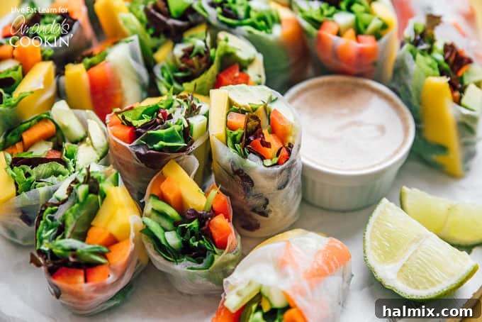 Fresh Vegetable Spring Rolls are made from colorful crisp vegetables and are a healthy appetizer that are perfect for summer! #springrolls #vegetable #veggierolls #summer #summerrecipes #potluck #avocado #jalapeno #appetizers #appetizerrecipes #vegetarian Vegetable spring rolls artfully arranged on a plate with a side of creamy dipping sauce, garnished with fresh lime wedges.
