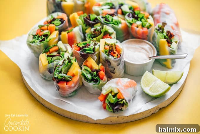 Fresh Vegetable Spring Rolls are made from colorful crisp vegetables and are a healthy appetizer that are perfect for summer! #springrolls #vegetable #veggierolls #summer #summerrecipes #potluck #avocado #jalapeno #appetizers #appetizerrecipes #vegetarian Beautifully arranged vegetable spring rolls on a plate, showcasing their colorful fillings, with a small bowl of dipping sauce on the side.
