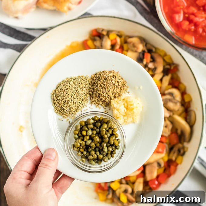 Dish with dried herbs and garlic for Chicken Cacciatore recipe. Minced garlic, capers, and dried Italian herbs measured out and ready to be added to the Cacciatore sauce.
