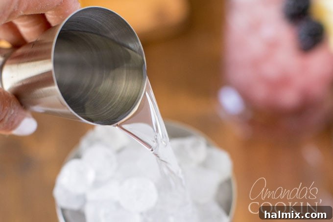 Bramble Bliss 4 Pouring gin into a cocktail shaker filled with ice, illustrating the first step of mixing the Bramble cocktail ingredients.