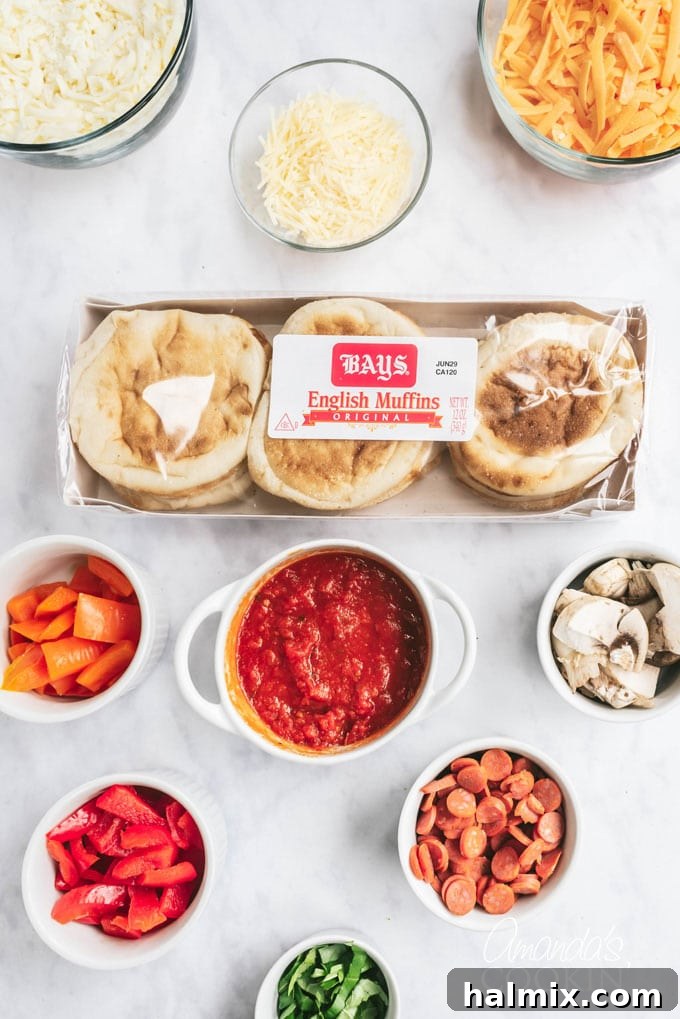 An array of fresh ingredients for English muffin pizzas laid out on a table, including muffins, sauce, cheese, and various toppings