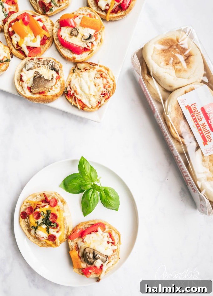 Two freshly baked English muffin pizzas on a white plate, with a tray of more pizzas in the background, ready for serving