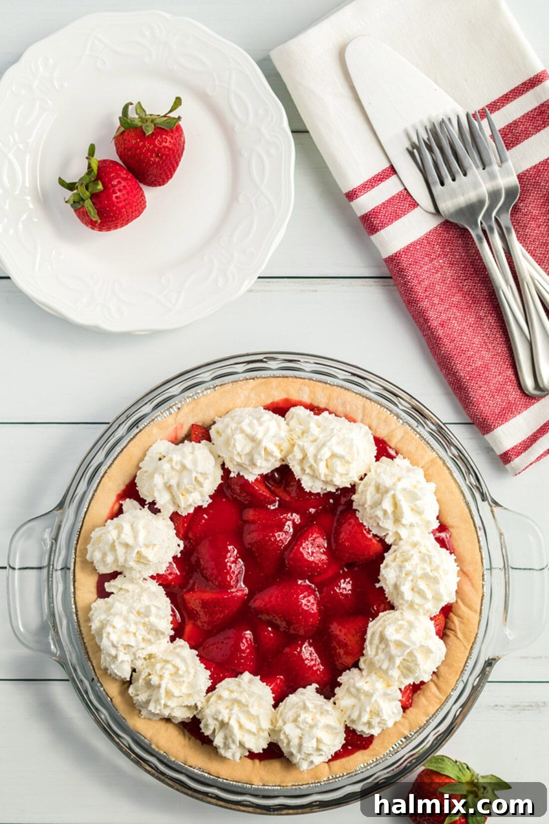 Fresh strawberry pie, generously decorated with a swirl of fluffy whipped cream, invitingly presented for serving.