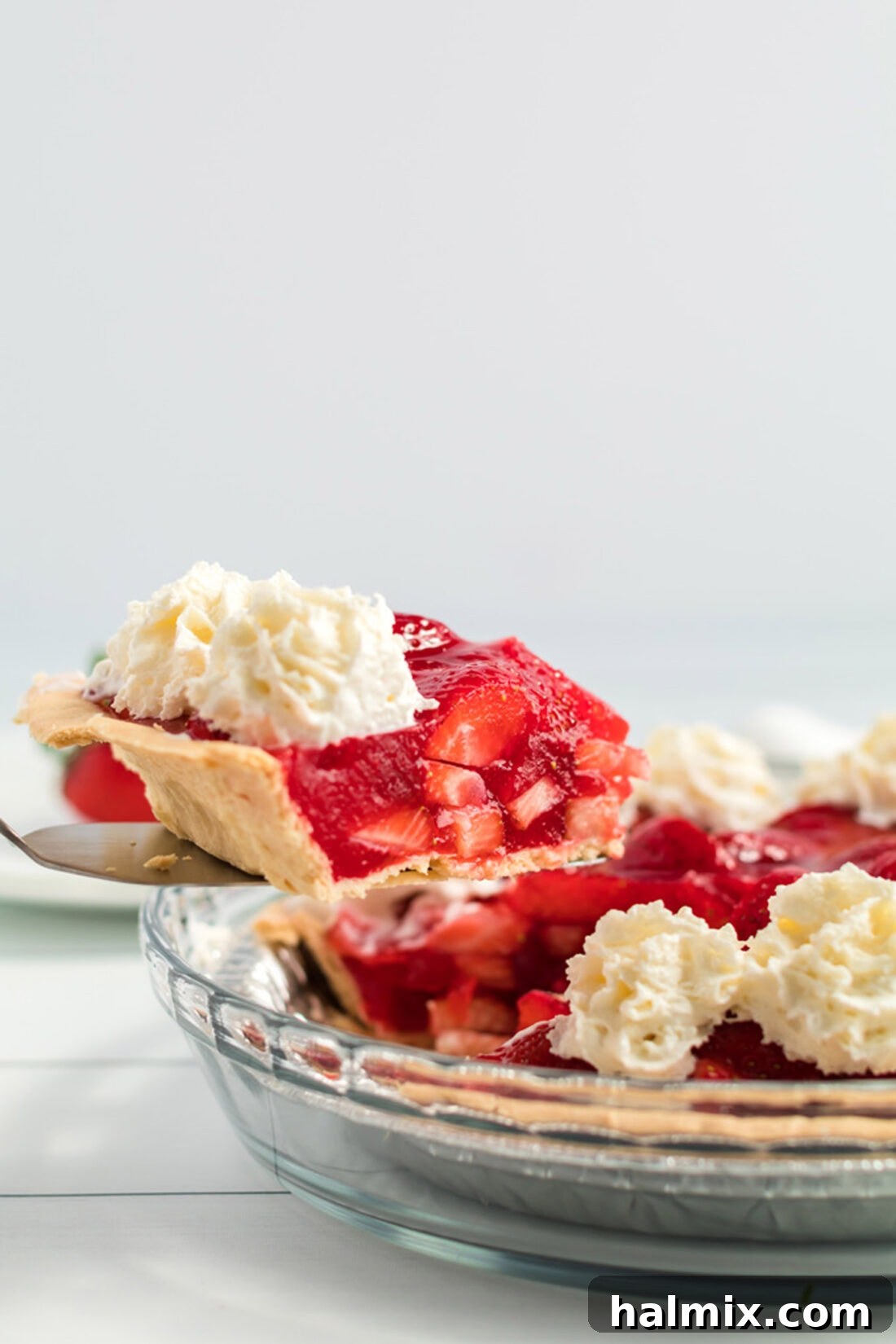 A server's hand delicately taking a generous slice of strawberry pie from the pie plate, revealing the rich, jello-infused berry filling.
