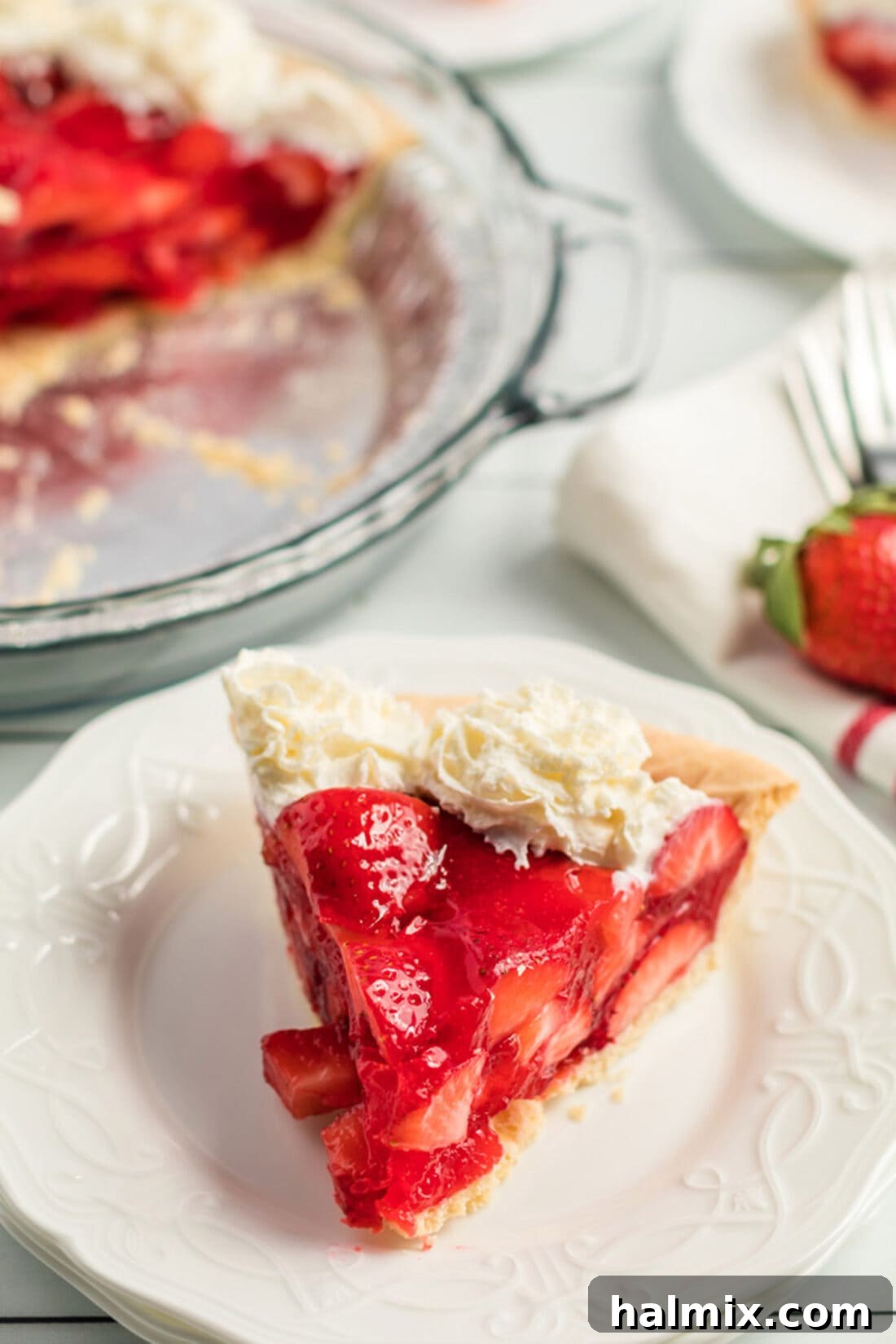A single, delectable slice of strawberry pie presented on a white plate, showcasing its vibrant berry filling and a dollop of whipped cream.