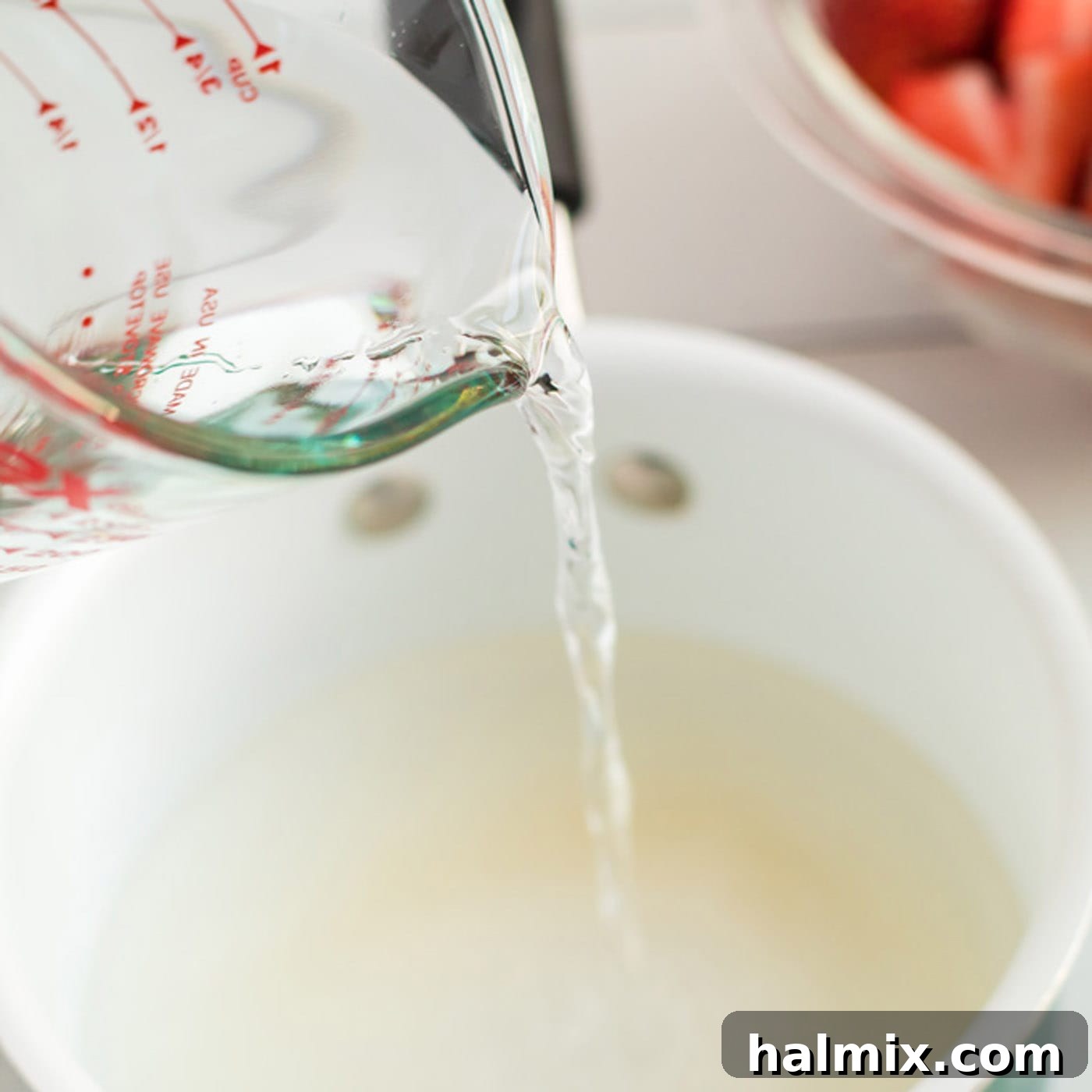 Water being poured into a bowl containing a mixture of sugar and cornstarch, to create the strawberry pie filling base.