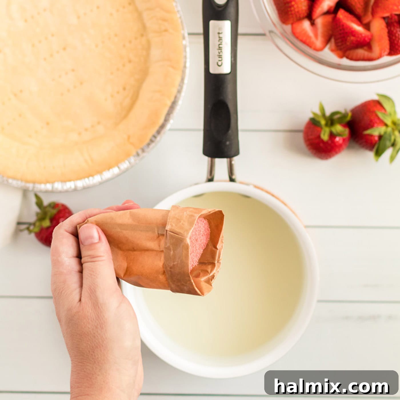 Strawberry jello powder being poured into the hot sugar and cornstarch mixture in a saucepan, ready to be stirred until dissolved.