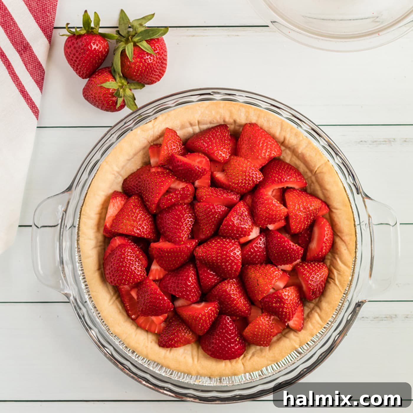 Freshly sliced and quartered strawberries neatly arranged within a baked and cooled pie crust, ready for the gelatin filling.