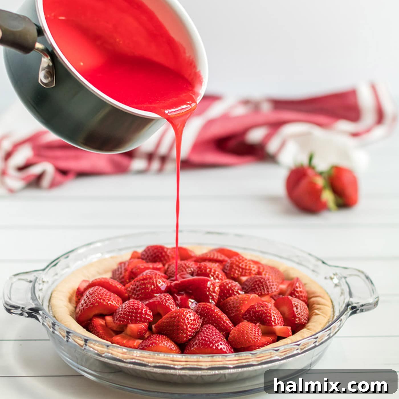 The vibrant red gelatin mixture being gently poured over the fresh strawberry slices already arranged in the baked pie crust.