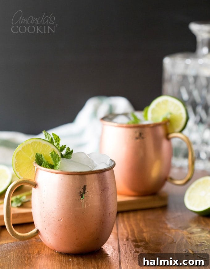 Two frosty copper mugs of Moscow Mule garnished with lime and mint
