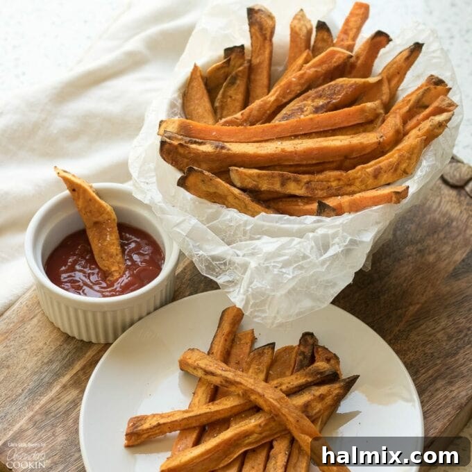 Baked Sweet Potato Fries on a white plate with a side of bright red ketchup, garnished with a sprig of fresh rosemary.