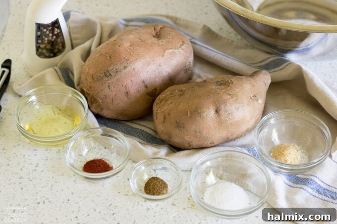 A flat lay of fresh sweet potatoes, measuring spoons, and small bowls containing smoked paprika, cumin, onion powder, Kosher salt, and pepper, showcasing all the ingredients needed for the recipe.