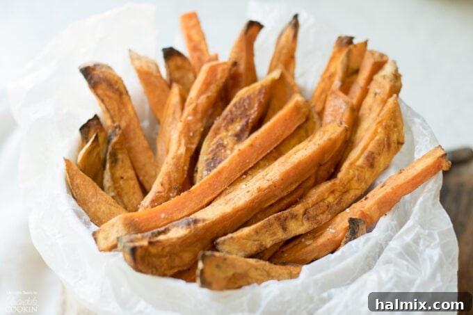 A close-up shot of perfectly baked sweet potato fries, seasoned and golden brown, piled on a parchment-lined baking sheet.