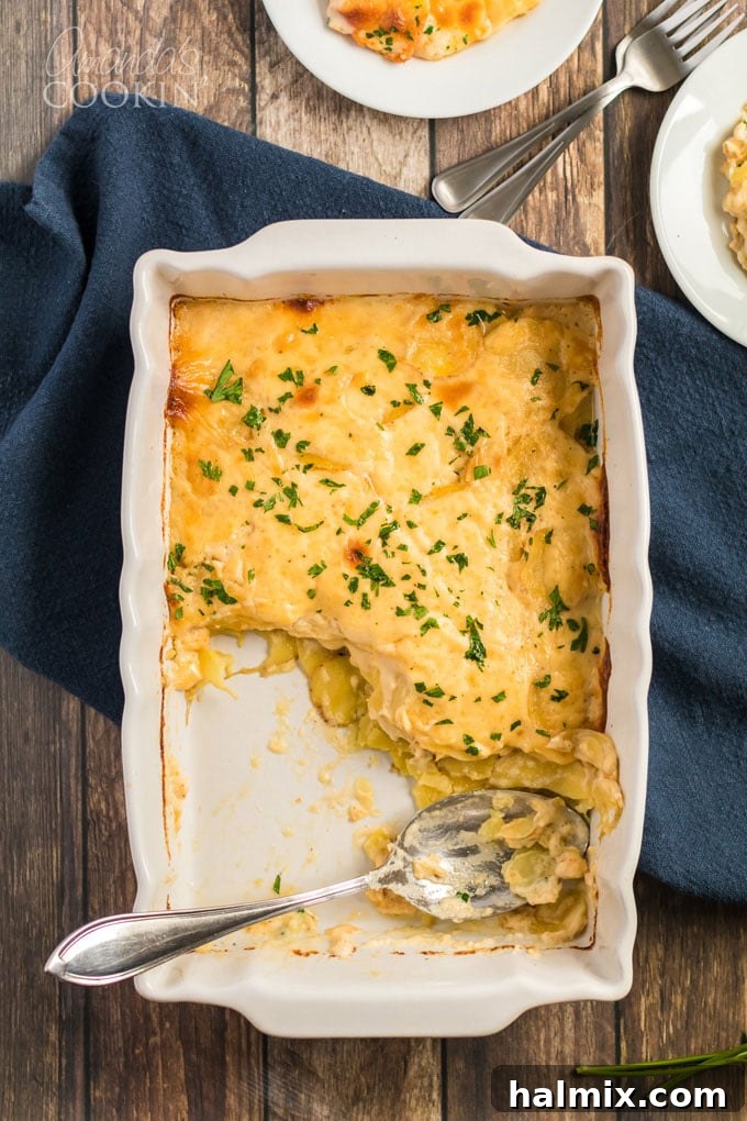 A panoramic view of a baking dish filled with golden-brown Au Gratin Potatoes, with a section already served, a spoon still in the pan, showcasing layers of tender potatoes and melted cheese.