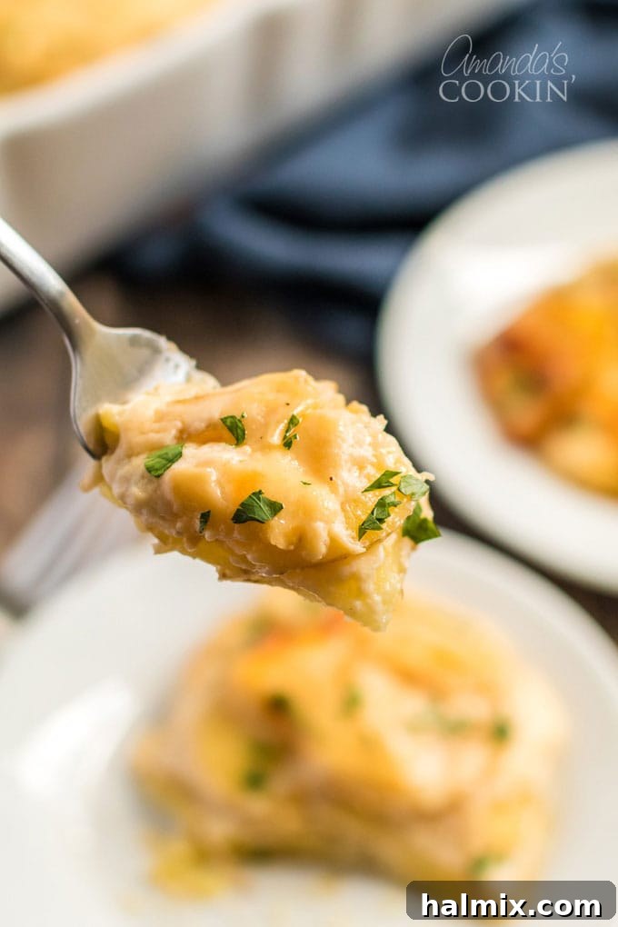 A serving spoon lifting a portion of cheesy scalloped potatoes from the pan, highlighting the layers of potatoes and creamy sauce.