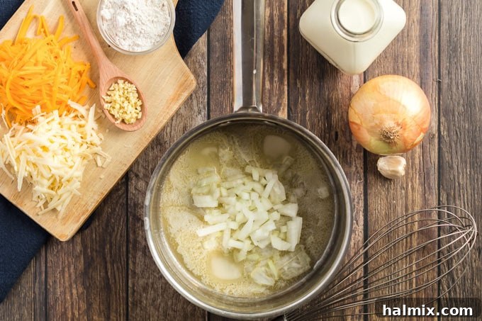 Close-up of a saucepan containing melted butter and gently sautéing chopped yellow onions, softening for the cheese sauce.