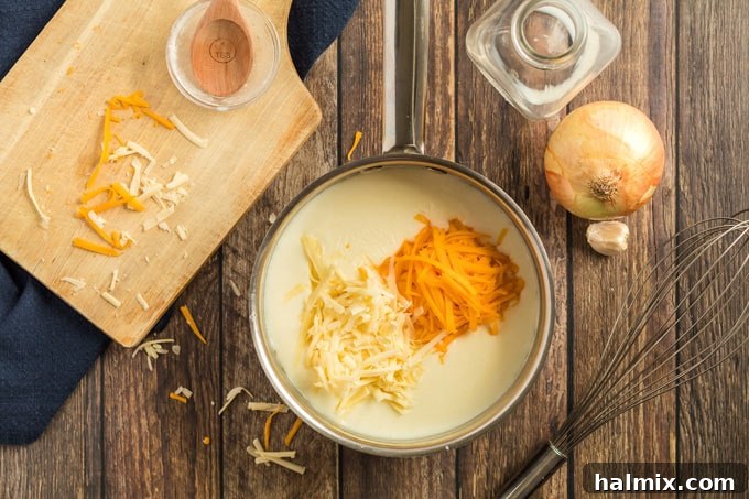 Close-up of shredded cheddar cheese melting into a creamy white sauce in a saucepan, being stirred until smooth.