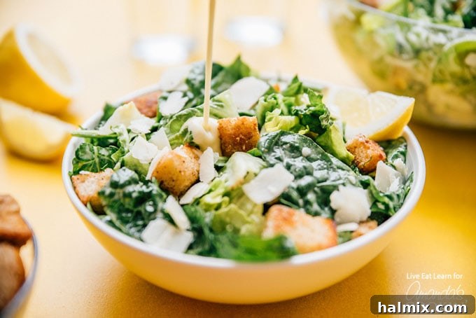 A large bowl of fresh romaine lettuce and golden croutons, with Caesar dressing being drizzled over the top