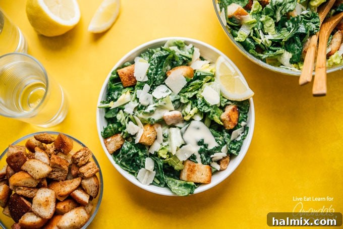 A fully assembled bowl of Caesar salad, garnished with extra shaved Parmesan and a lemon wedge, placed on a wooden table
