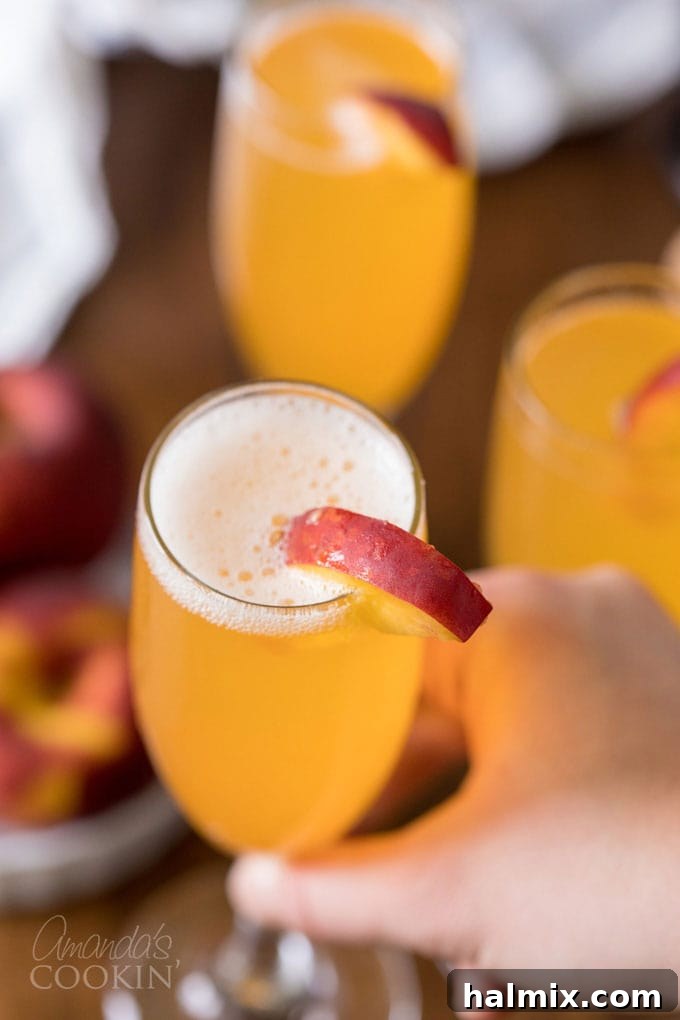 A hand lifting a sparkling Bellini cocktail in a champagne flute, ready to be enjoyed.