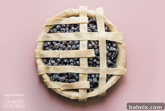 Close-up of hands expertly weaving dough strips to create a classic lattice pattern over a blueberry pie filling in a pie dish.
