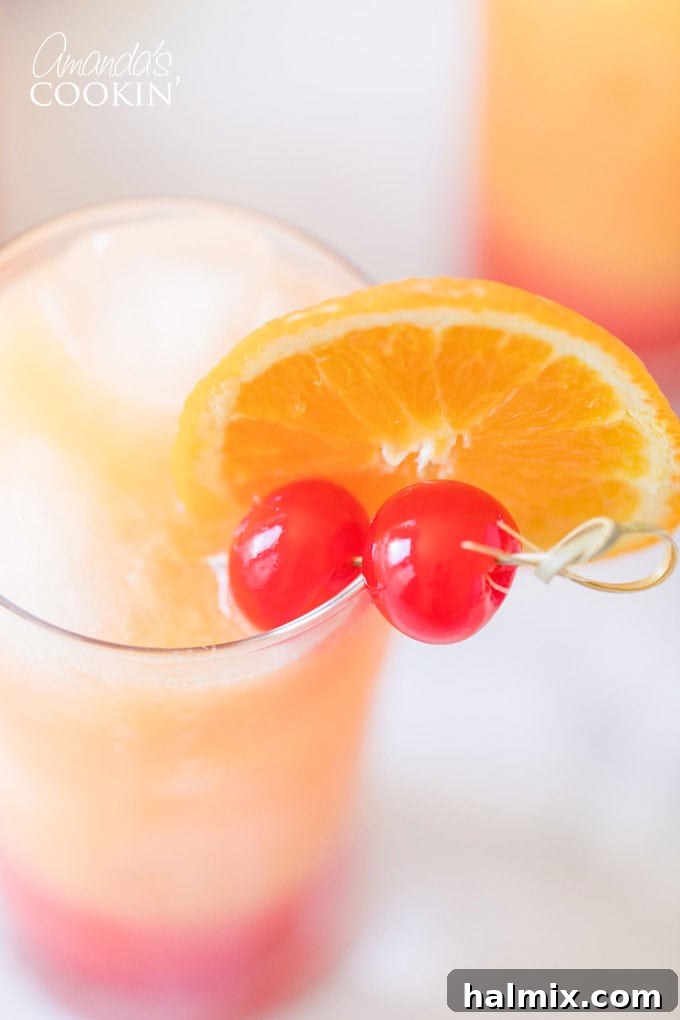 Close up of a Tequila Sunrise cocktail with orange and cherry garnishes.