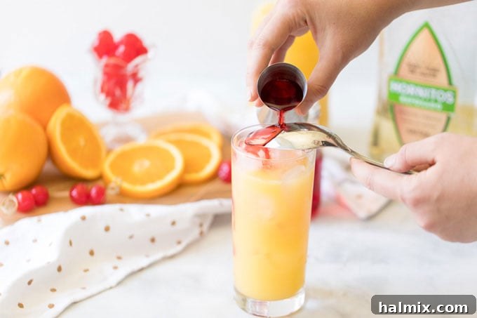 Pouring grenadine syrup over the back of a spoon into a Tequila Sunrise glass to create layers.