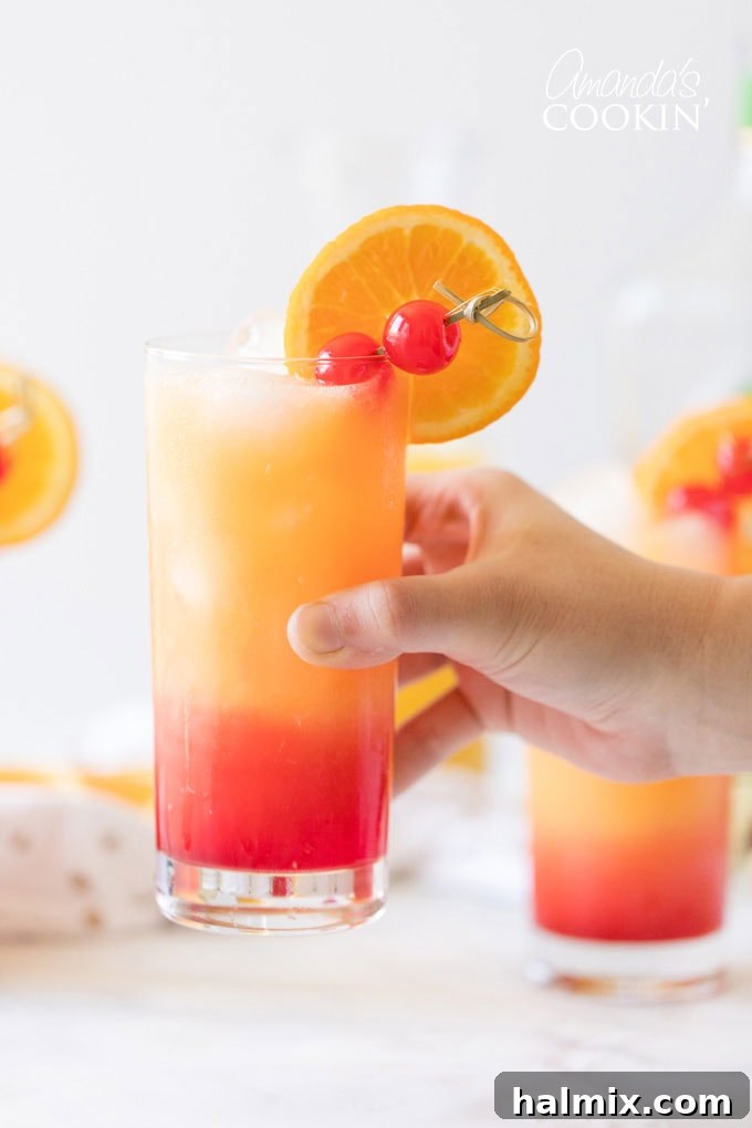 A hand holding a vibrant Tequila Sunrise drink, showcasing its beautiful layers.