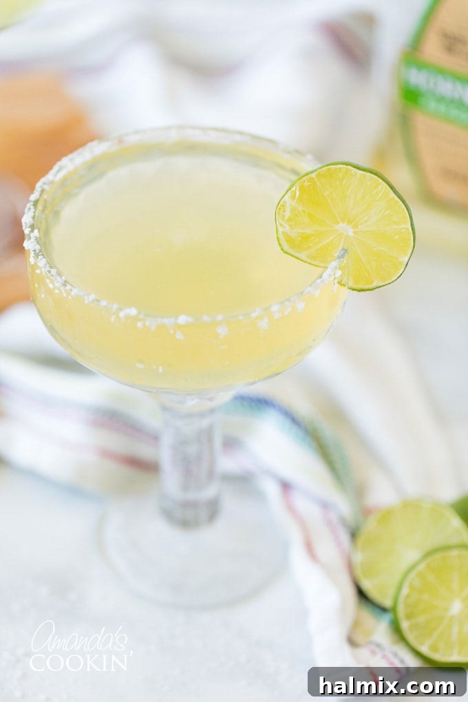 The pure elegance of a Margarita served 'up' in a chilled glass, highlighting its smooth texture and vibrant color. A Margarita cocktail, served without ice in a chilled coupe glass, garnished with a lime wheel