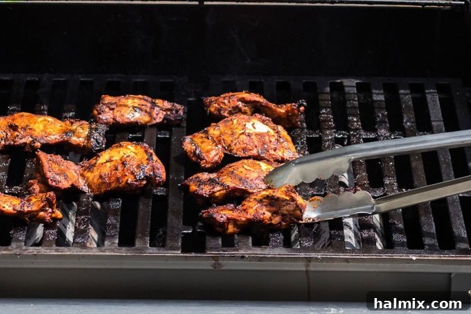 Two chicken thighs sizzling on a hot grill, showing developing char marks.