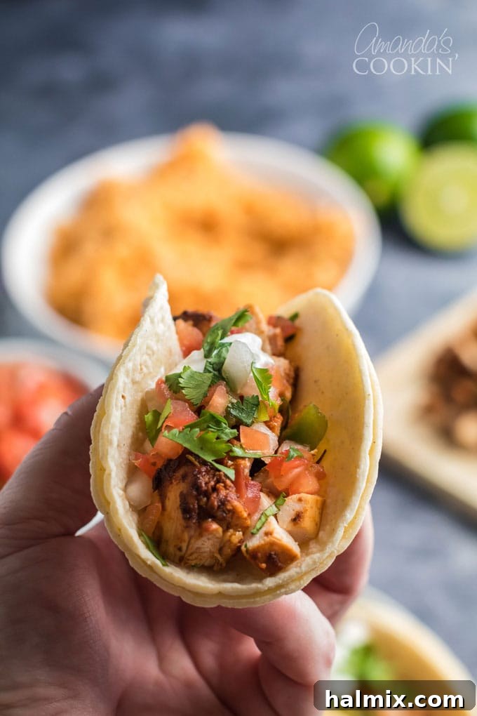 A hand holding a perfectly assembled chicken taco with vibrant toppings, ready to be eaten.