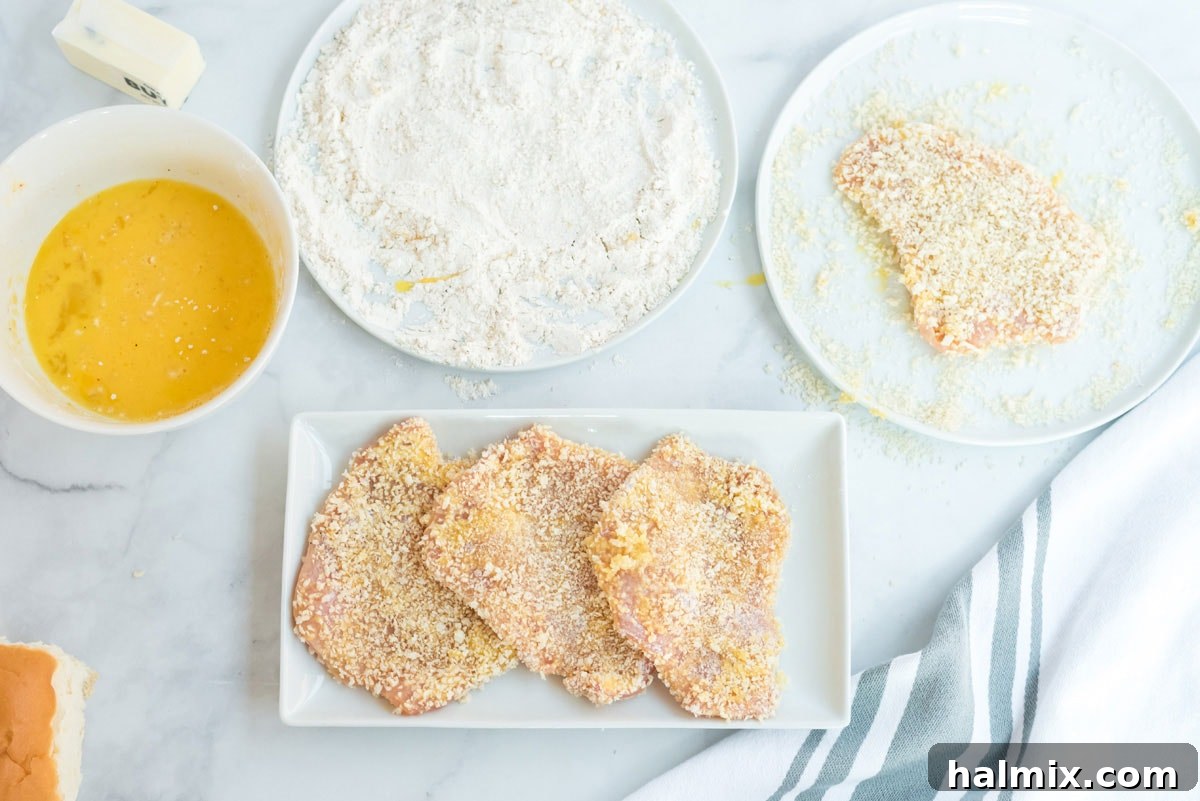 Three perfectly breaded pork chops arranged on a plate, showcasing their even coating before frying.