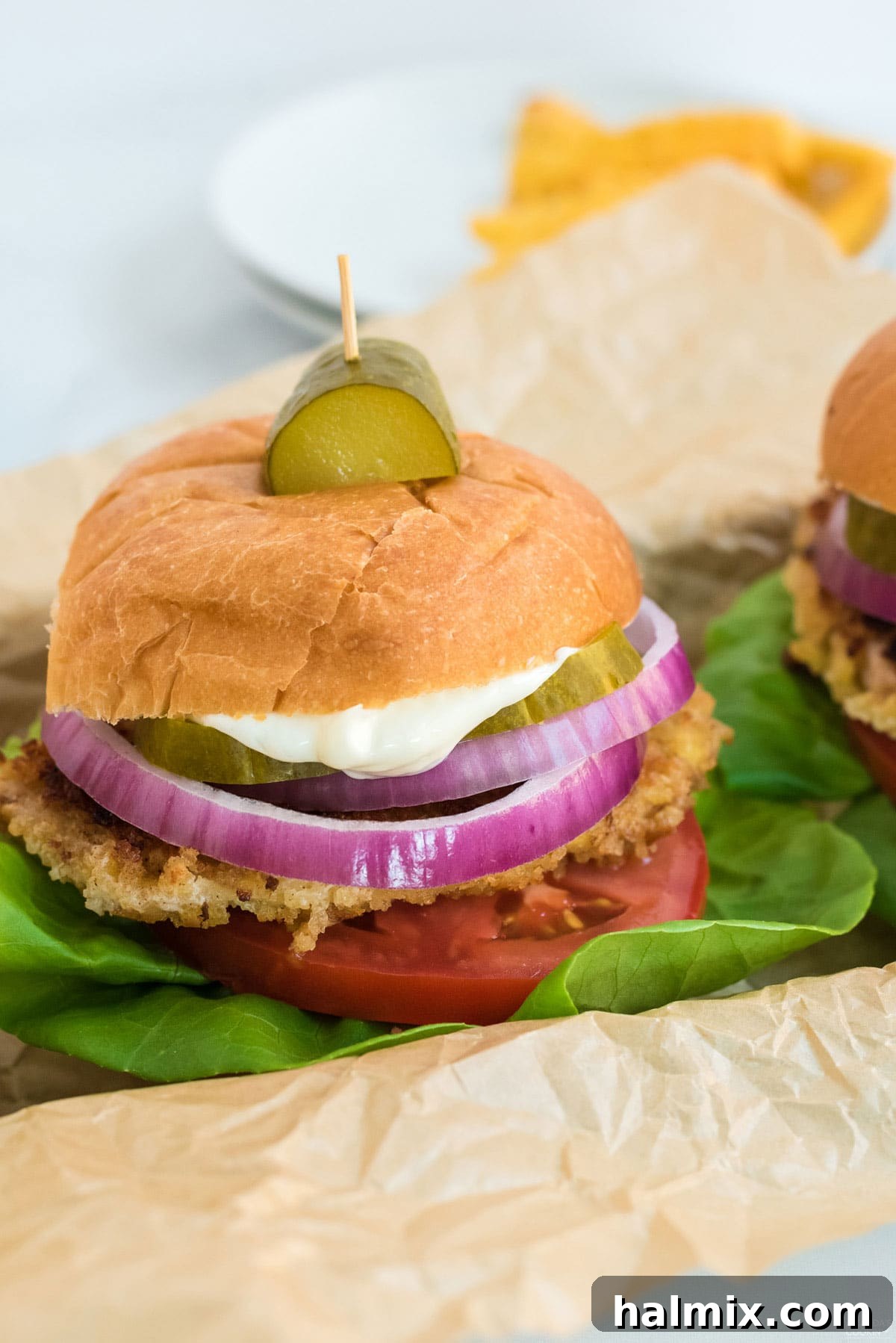 A close-up of a delicious Iowa pork tenderloin sandwich, beautifully assembled with fresh toppings and a pickle garnish.