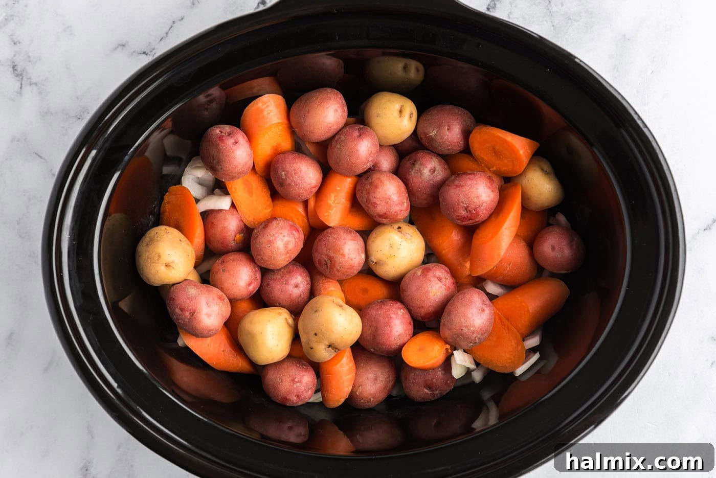 Perfect Slow Cooker Pot Roast 6 baby potatoes and carrots added on top of onions in slow cooker crock