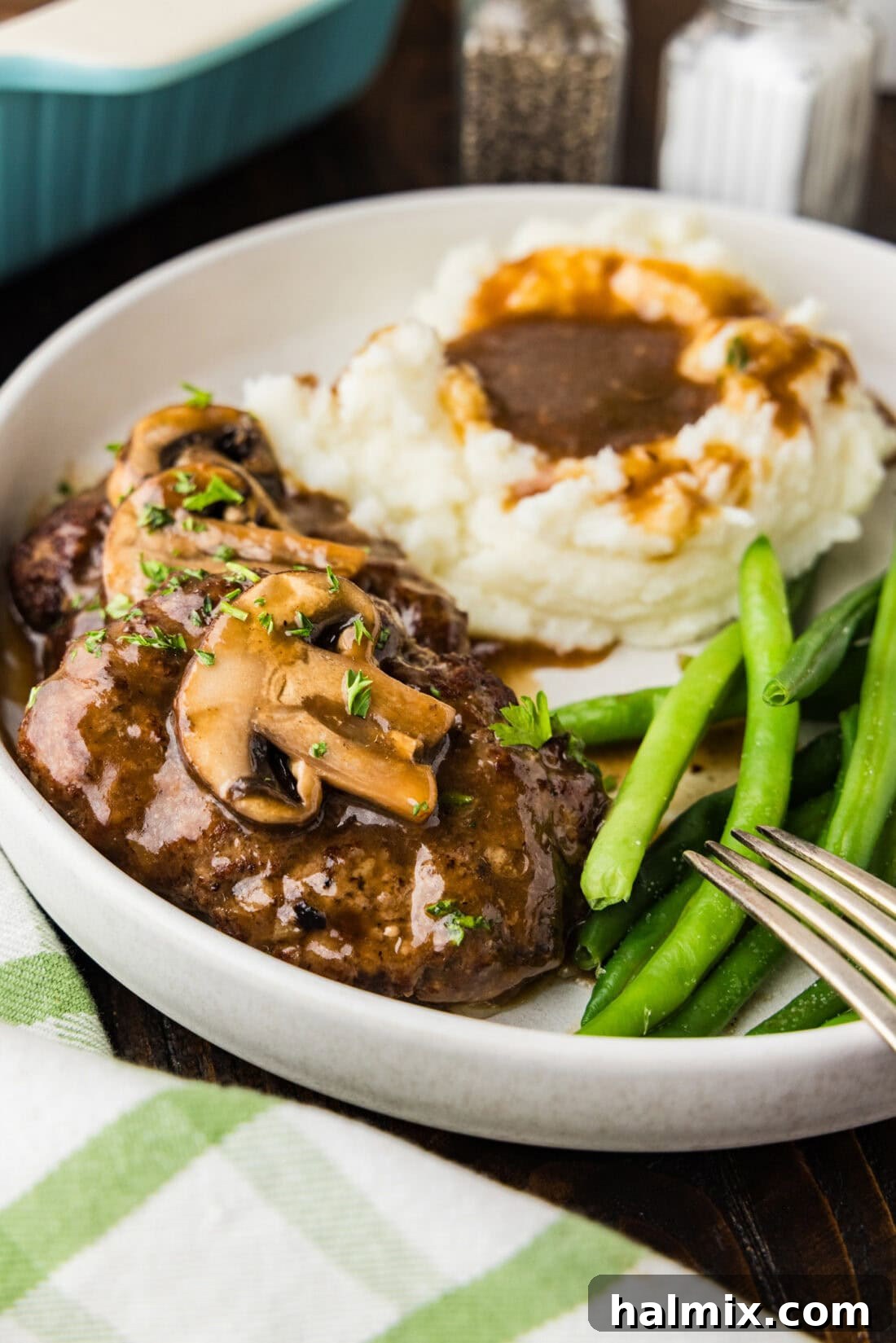 Hearty Salisbury Steaks 2 Salisbury steak on a plate with mashed potatoes and green beans, a classic comfort food meal.
