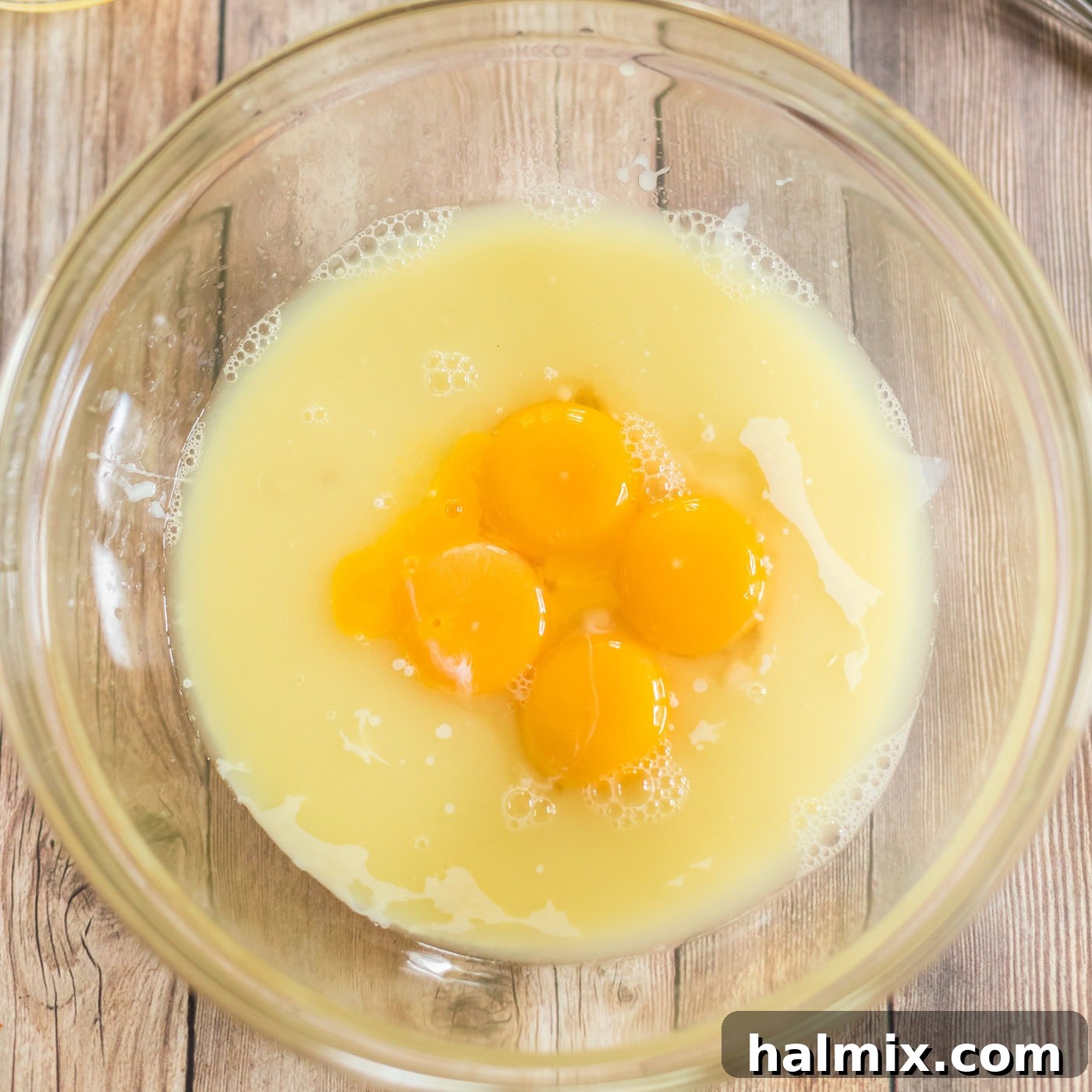 A bowl containing sweetened condensed milk and egg yolks, being whisked together for the pie filling