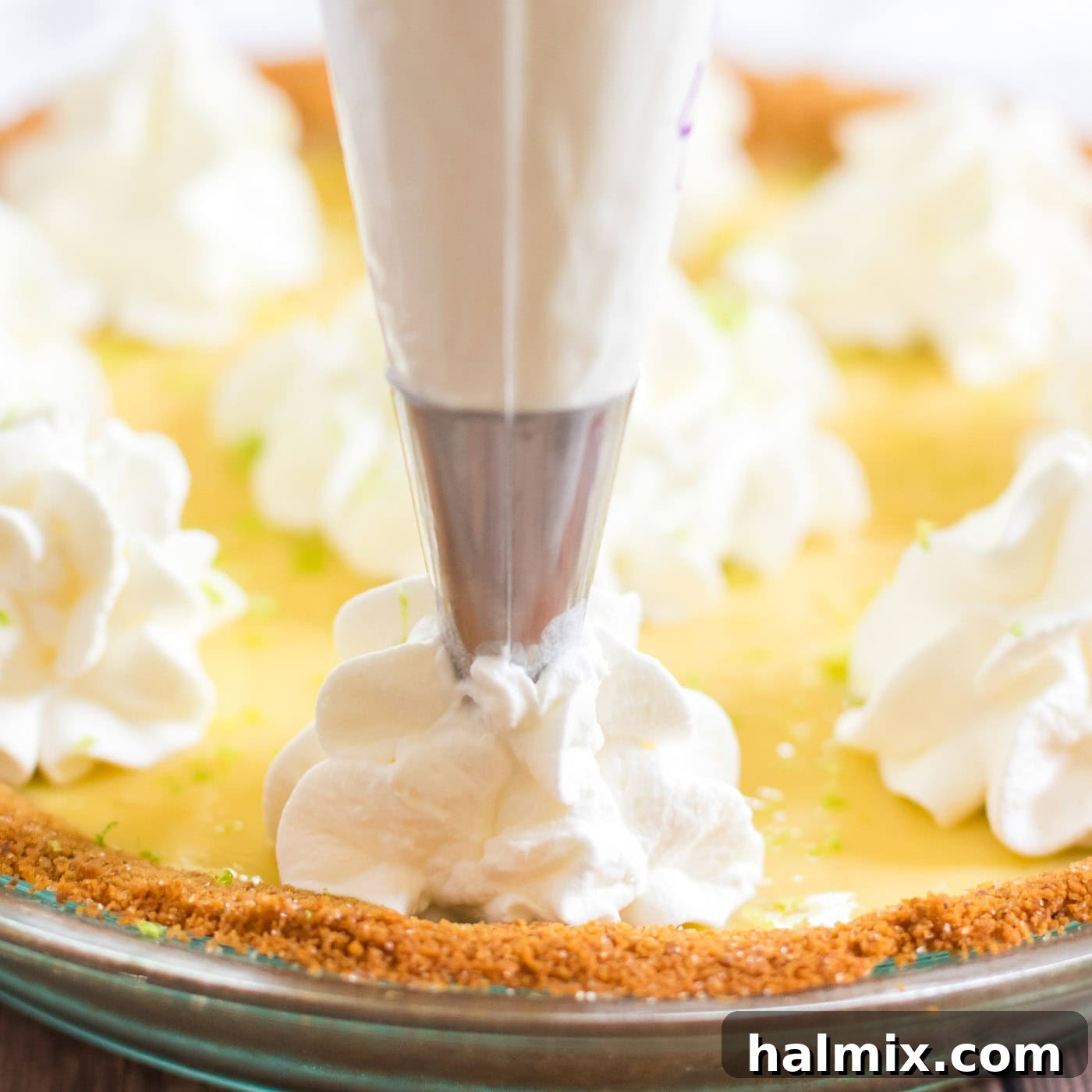 A baker piping fresh whipped cream onto the edge of a Key Lime Pie, adding a beautiful finishing touch
