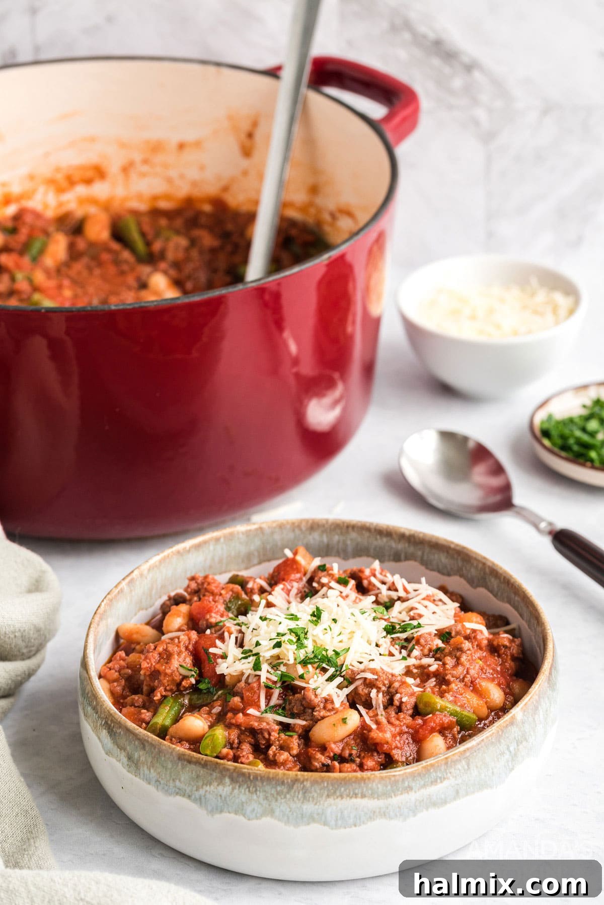 A steaming bowl of Italian Hamburger Stew, garnished with fresh herbs and Parmesan, with a rustic pan in the soft-focus background.
