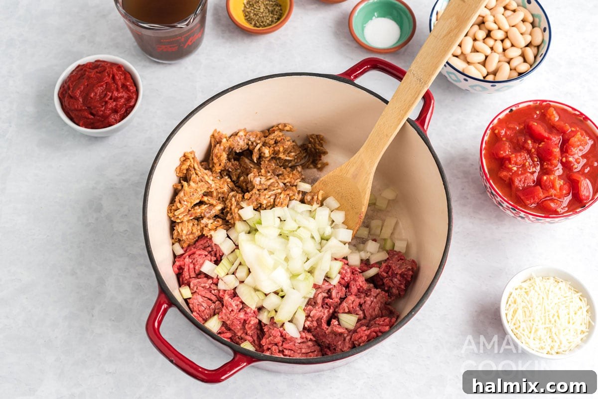 Ground beef, Italian sausage, and chopped onions browning together in a large Dutch oven, preparing the base for the stew.