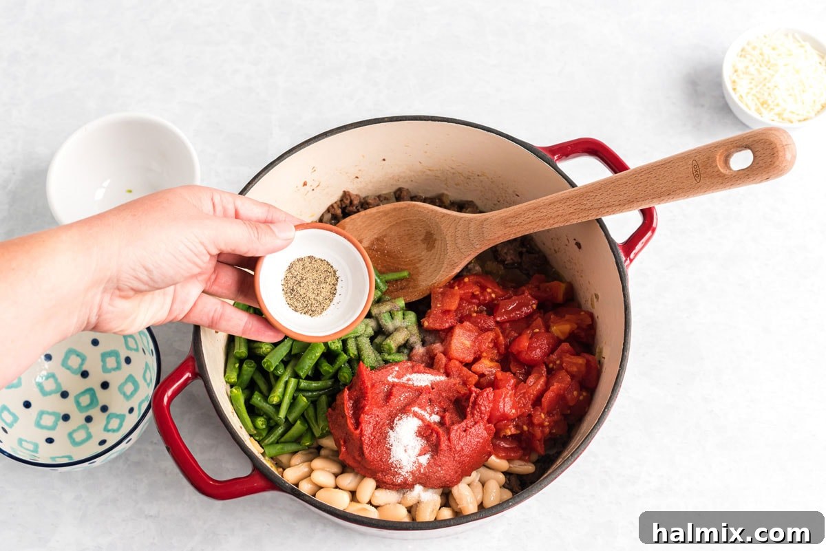 Dried oregano, salt, and pepper being sprinkled into the pot of stew ingredients, adding the final seasoning touches.