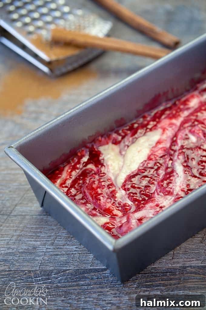 A loaf pan filled with the light-colored coffee cake batter, topped with a vibrant red raspberry filling, swirled into the batter.